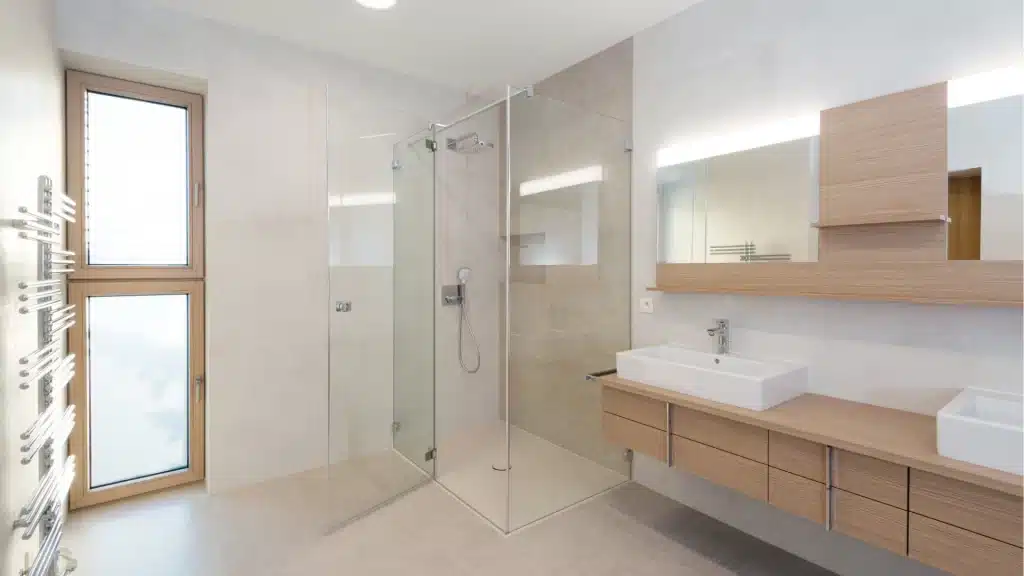 Modern bathroom remodel with frameless glass shower enclosure, wooden vanity, and vessel sinks