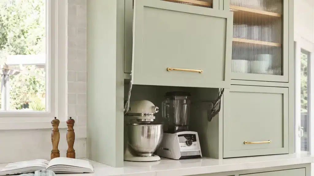 Sage green kitchen cabinet with a vertical lift-up door open, revealing a stand mixer and blender stored inside.