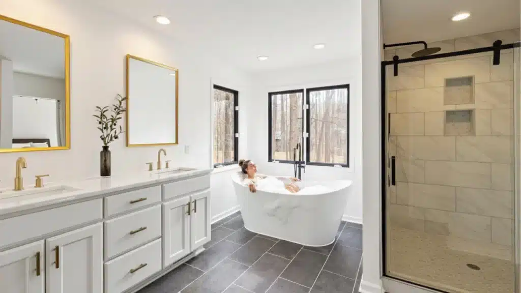 Modern master bathroom with white vanity, freestanding soaking tub, walk-in shower, and black framed windows by Pottstown Construction