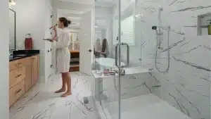 Modern primary bathroom remodel with marble tile flooring, frameless glass shower enclosure, and wood vanity cabinet with black countertop