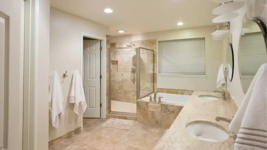 Existing bathroom with beige tile, double vanity, soaking tub, and enclosed shower
