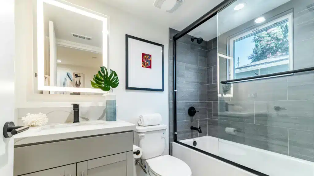 Bright bathroom remodel with lit mirror, tub shower, and black tile accents