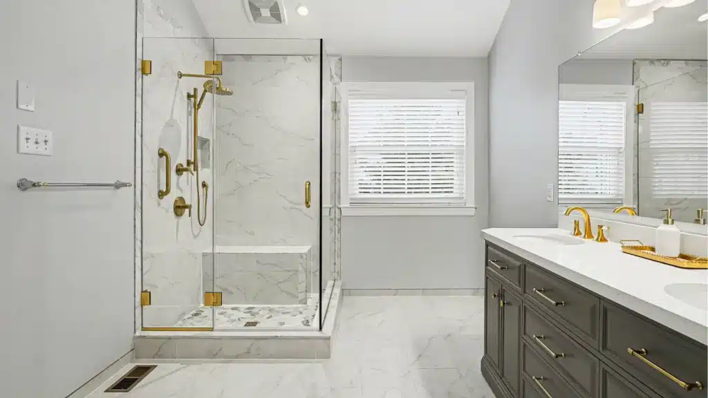 Bathroom remodel with gray vanity and marble shower with gold fixtures