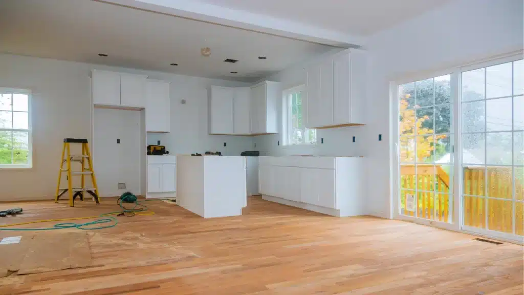 Kitchen remodel in progress with white cabinets, hardwood flooring, and large windows during construction