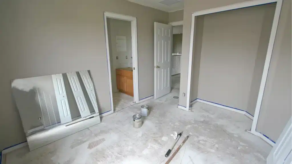 Unfinished bathroom remodel space with removed flooring, paint cans, and mirror