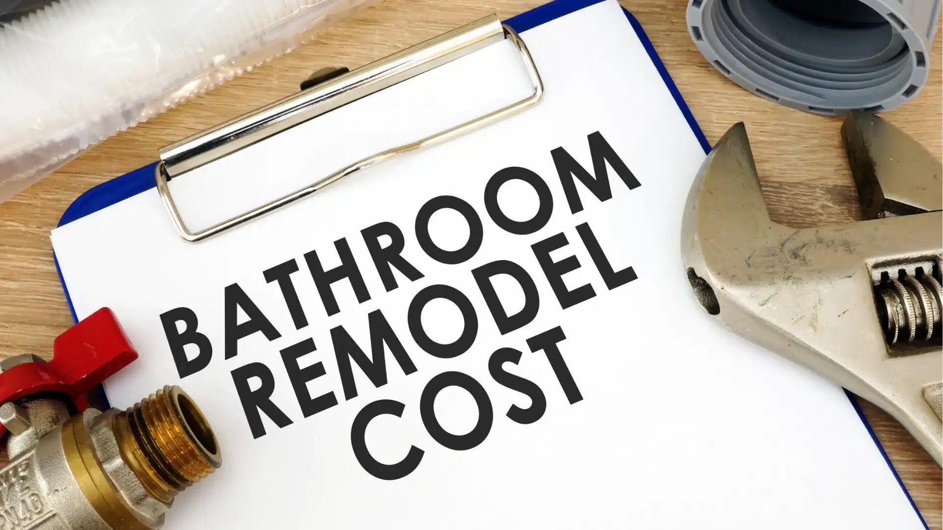 Blog 61 Bathroom remodel cost text on clipboard beside pipe fittings and wrench