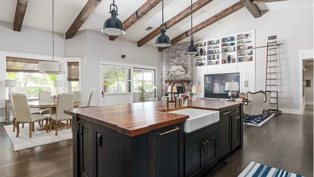 Modern open-concept kitchen and living room with black island, wood beams, brick fireplace, and built-in shelving