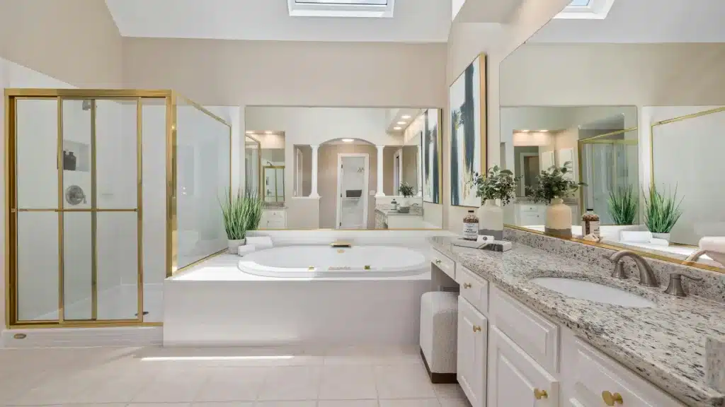 Spacious primary bathroom with skylight, gold-framed glass shower, drop-in jetted tub, and granite double vanity